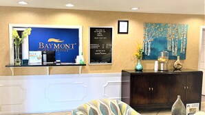 Een receptiegedeelte met een Baymont Inn bord, een ingelijste welkomstboodschap, een kaart van de omgeving en een decoratief schilderij.