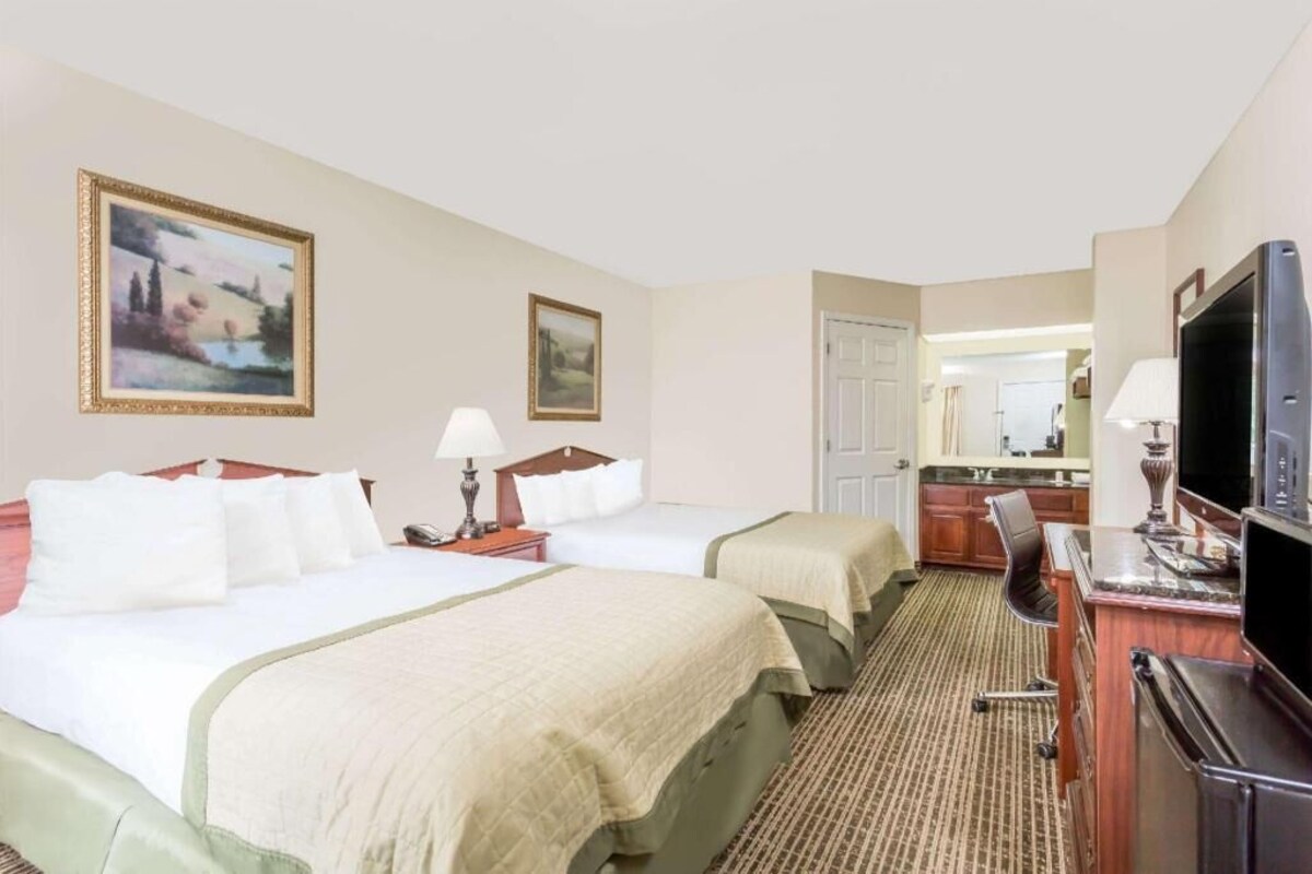 A hotel room with two beds, a desk, a television, and a kitchen area.