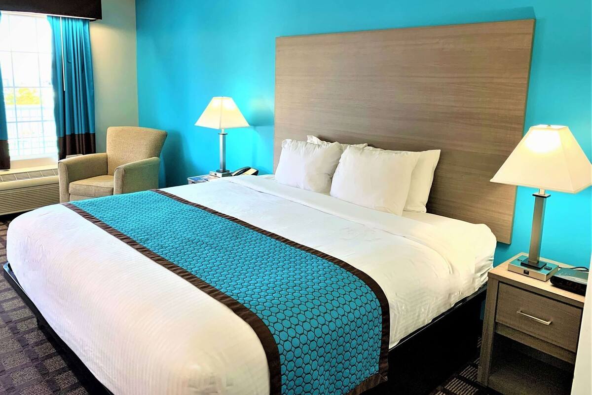 Une chambre d’hôtel avec un lit, deux lampes de chevet, une chaise, une table de chevet et une fenêtre avec des rideaux.