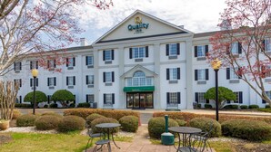 A hotel with a classic design, featuring a central entrance, a green awning, and a well-maintained outdoor seating area with tables and chairs.