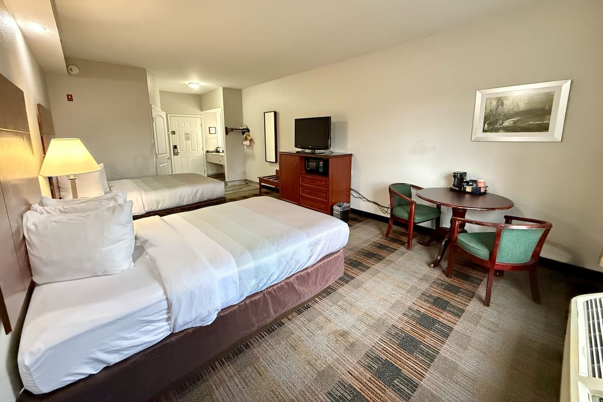 Habitación de hotel con dos camas, un escritorio, una silla, un televisor y una pequeña mesa con cafetera.