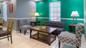 A room with a green accent wall, a grey sofa, patterned chairs, a wooden coffee table, and two lamps.