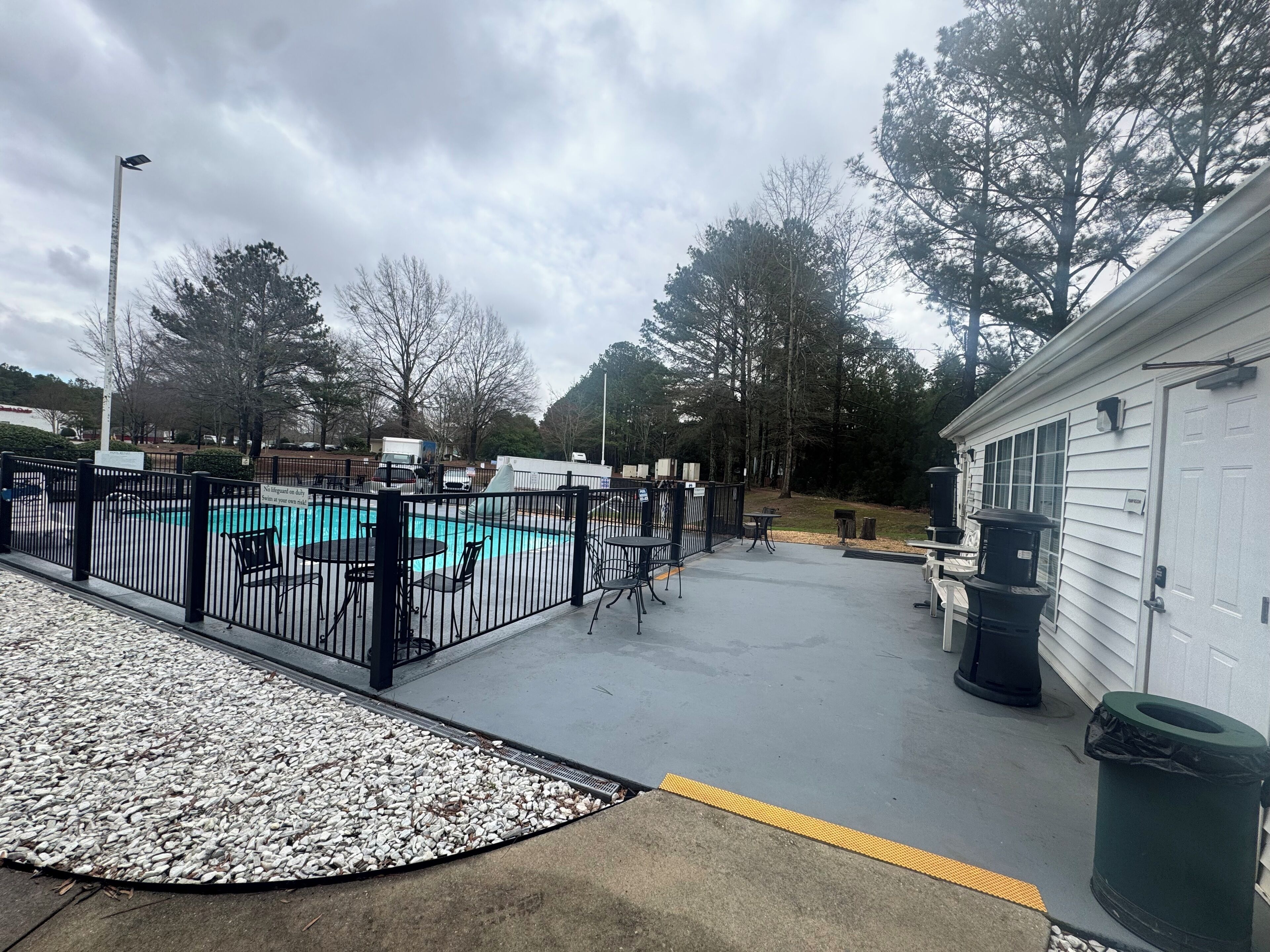 A swimming pool area with a fenced deck, outdoor seating, and a trash can.