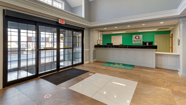 A hotel lobby with a glass door entrance, a reception desk, and a green sign indicating a quality service area.