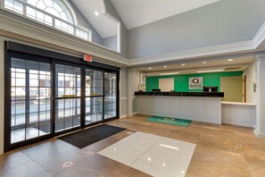 Un hall d’hôtel avec une entrée dotée d’une porte en verre, un comptoir d’accueil et un panneau vert indiquant une zone où sont offerts des services de qualité.