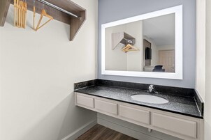 Un baño con un espejo grande, un lavabo y perchas de madera en un perchero.