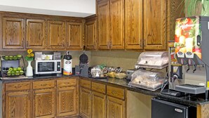 A kitchen with wooden cabinets, a microwave, a coffee machine, and various food items. - Baymont by Wyndham Sanford (Sanford)