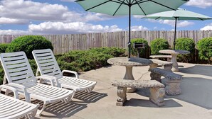 An outdoor patio with white lounge chairs, a large umbrella, and decorative stone tables. - Baymont by Wyndham Sanford (Sanford)