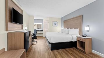 Habitación de hotel con cama, mesita de noche, escritorio, silla y televisor en la pared.