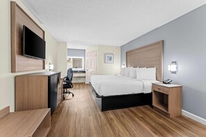 Habitación de hotel con cama, mesita de noche, escritorio, silla y televisor en la pared.