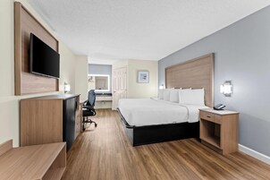 Habitación de hotel con cama, mesita de noche, escritorio, silla y televisor en la pared.