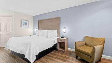 A hotel room with a bed, bedside table, chair, and a painting on the wall.