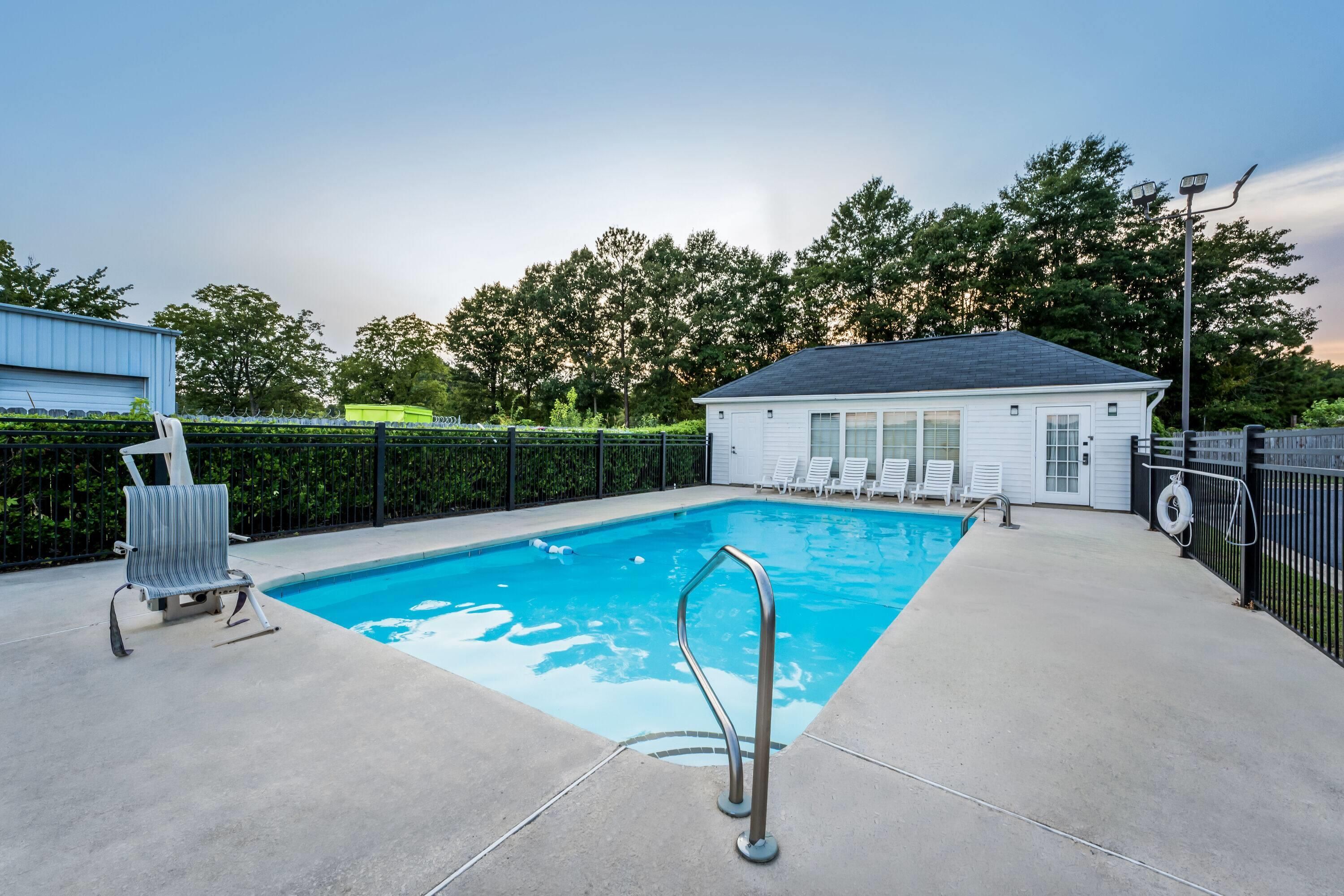 A swimming pool with a metal ladder, surrounded by a fence, with a building and trees in the background.