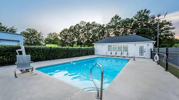A swimming pool with a metal ladder, surrounded by a fence, with a building and trees in the background.