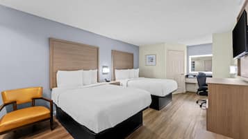 Ein Hotelzimmer mit zwei Betten, einem Schreibtisch, einem Sessel und einem Fernseher.