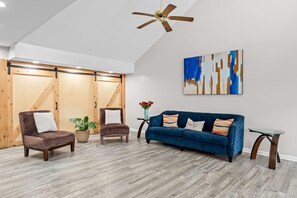 Una sala de estar moderna con piso de madera, un sofá azul, dos sillones, una mesa de centro y un ventilador de techo.