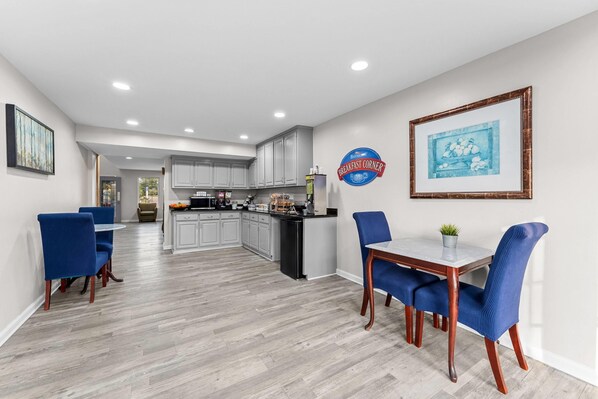 Una cocina moderna con armarios blancos, un comedor con sillas azules y un cartel que dice 'Desayuno' en la pared.