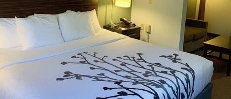 Una habitación de hotel con una cama grande, una mesita de noche con lámpara y una pared decorada con cuadros.
