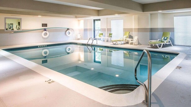 Una piscina interior con superficie de agua cristalina, un trampolín y sillones de descanso alrededor de la piscina.