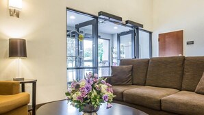 Un vestíbulo de hotel con un sofá, una mesa redonda con un florero, una lámpara y un gran ventanal con vistas.
