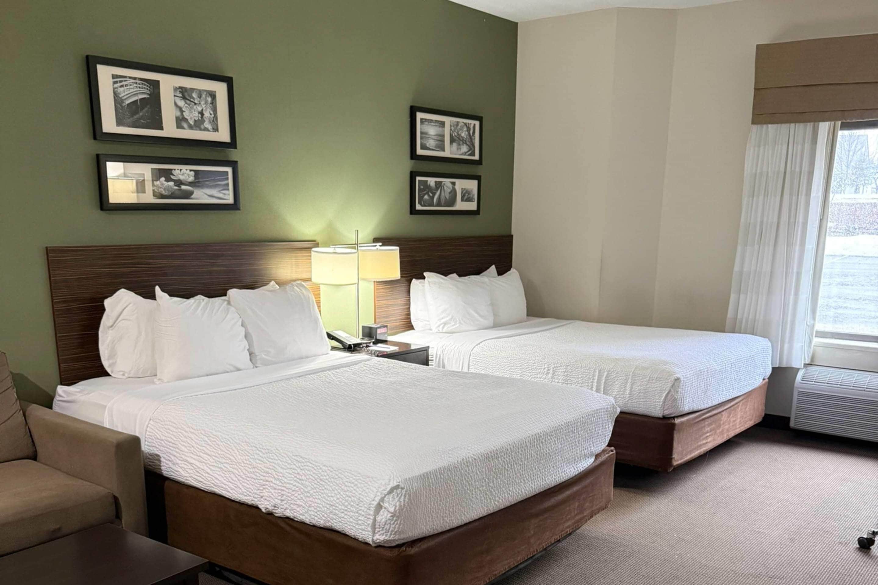 Una habitación de hotel con dos camas, un escritorio, una silla y cuadros en la pared.