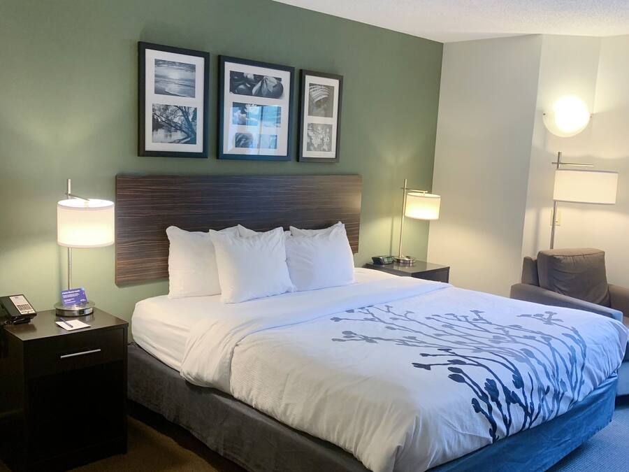 A hotel room with a large bed, two bedside tables, a nightstand, a chair, and three framed pictures on the wall.