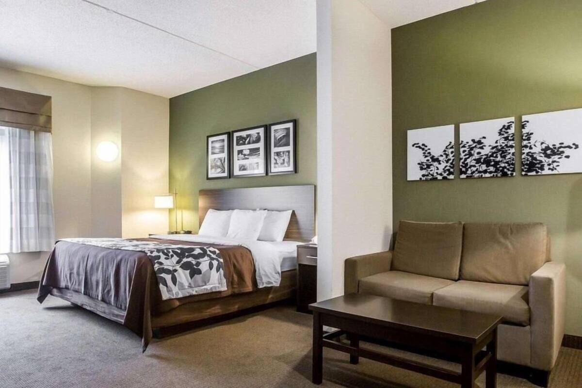 A hotel room with a bed, a sofa, a coffee table, and artwork on the walls.