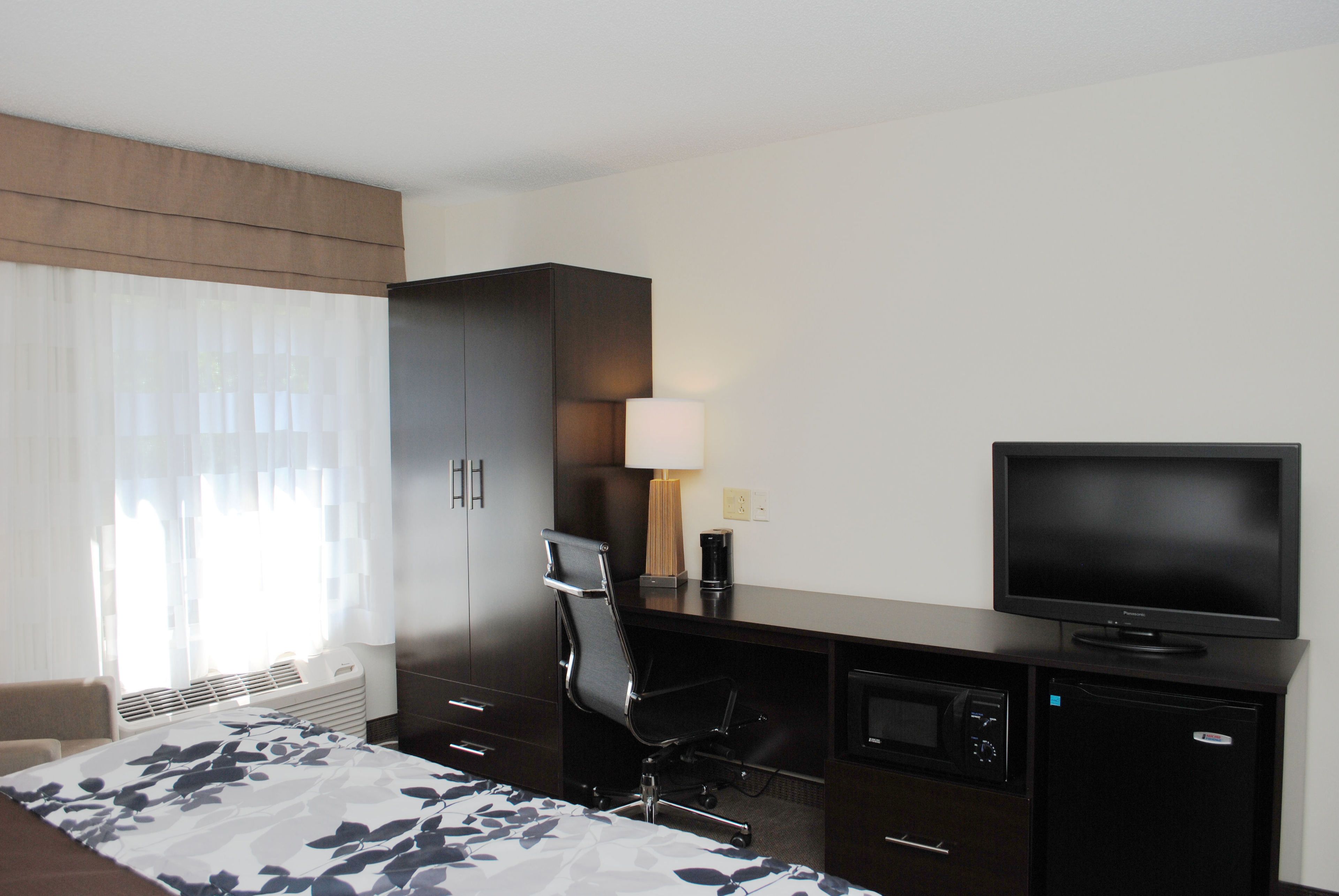 A hotel room with a bed, a desk, a chair, a television, a lamp, and a microwave.