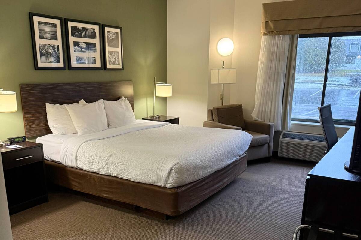 A hotel room with a large bed, a desk with a computer, a chair, a lamp, and framed pictures on the wall.