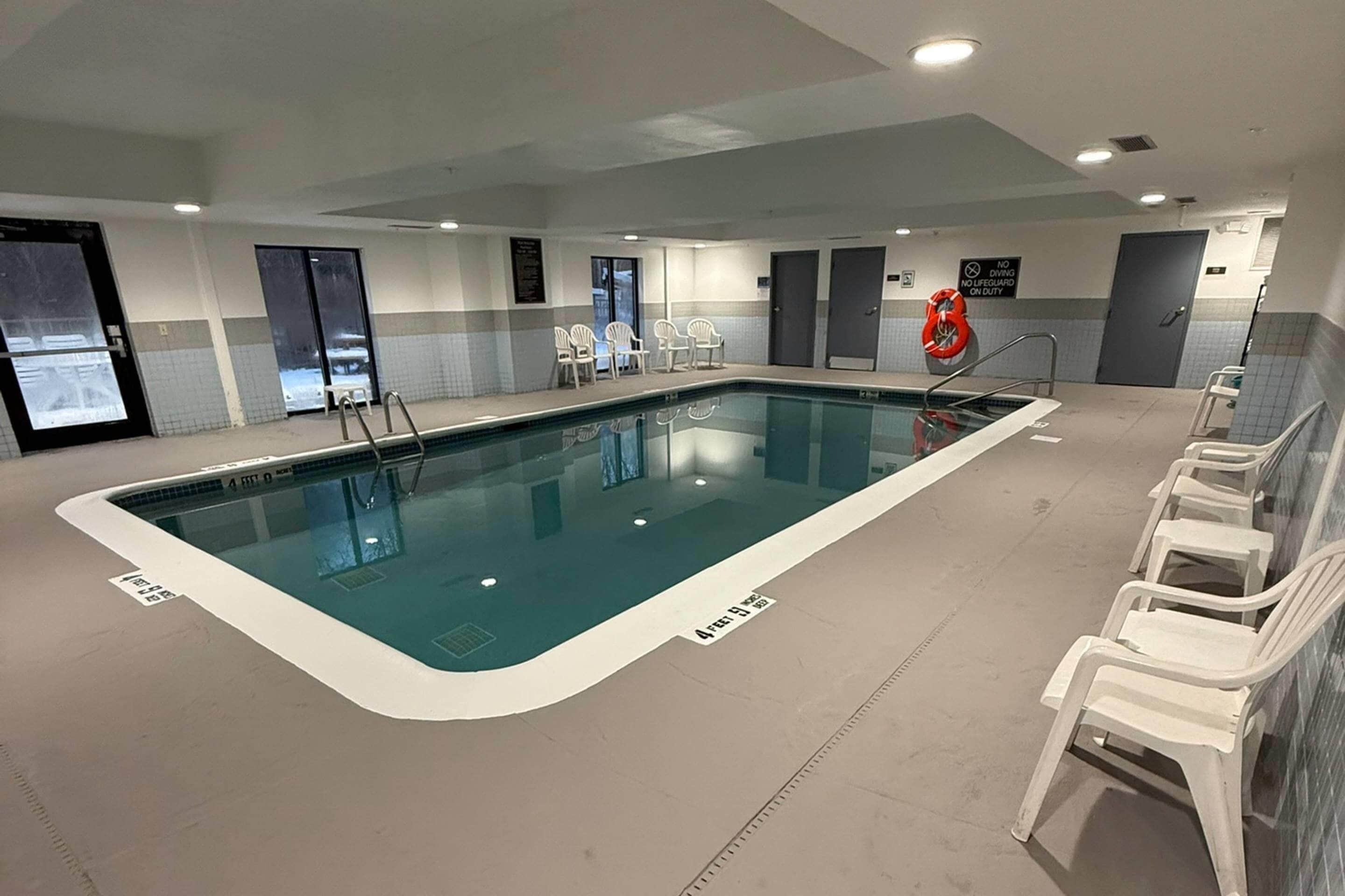 Une piscine intérieure à l’eau claire, entourée de chaises blanches, et une bouée de sauvetage fixée au mur.