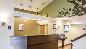Zona de recepción de hotel con un mostrador de madera, una mesa de registro y una escalera que lleva a un nivel superior.
