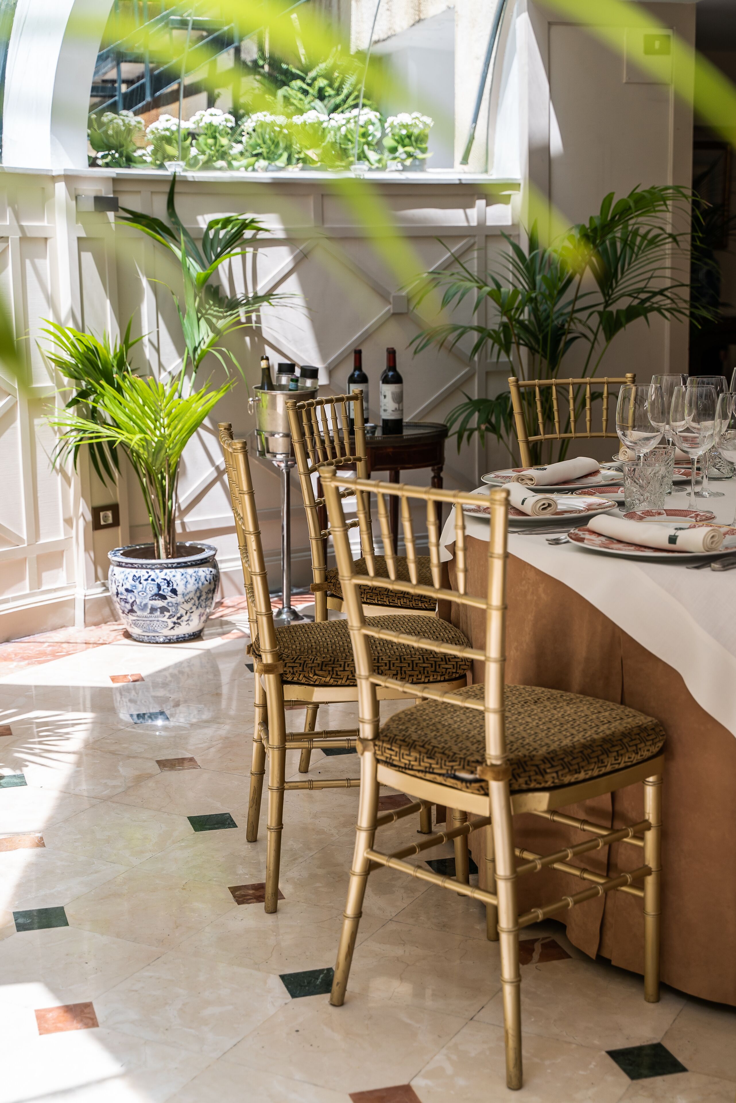 A dining area with a table set for four, bamboo chairs, a potted plant, and a view of a staircase.