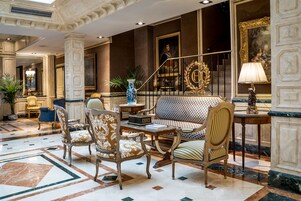 Un vest íbulo con muebles ornamentados, una escalera y un cuadro grande.