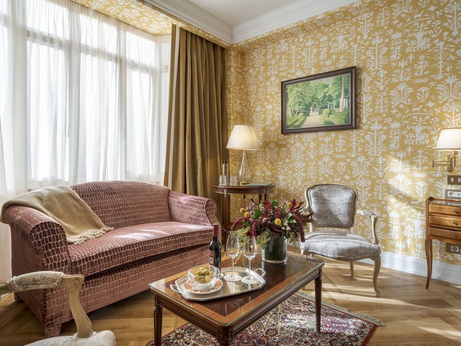 Una sala de estar con papel tapiz estampado, un sofá rojo, una mesa de centro de madera y una silla.
