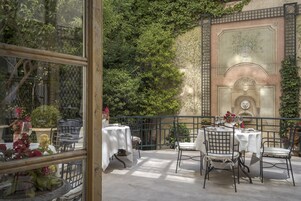 Un patio exterior con mesas y sillas, rodeado de vegetación y un muro decorativo.