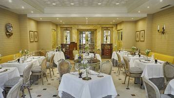 A formal dining room with multiple tables and chairs, each set with white tablecloths and silverware.