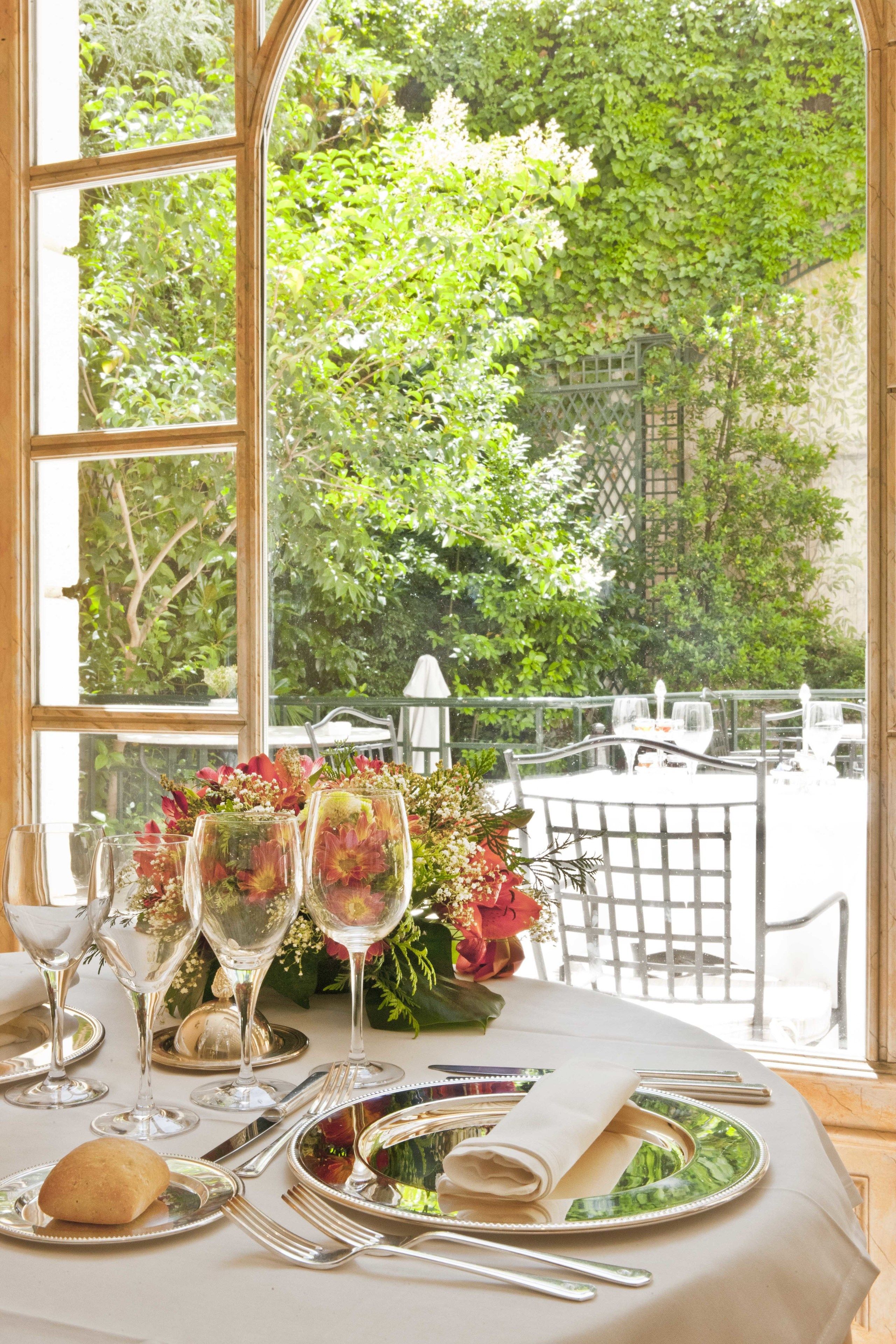 A table set for a meal with a view of a garden through a large window.