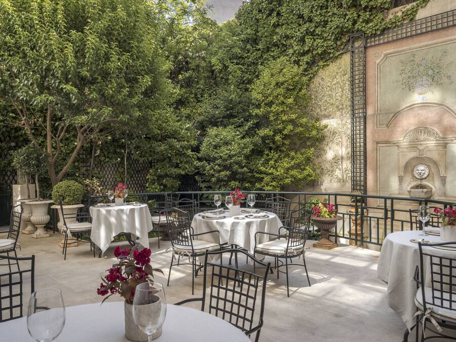 Eine Außenpatio mit runden Tischen und Stühlen, umgeben von üppiger Vegetation und einer Zierwand.