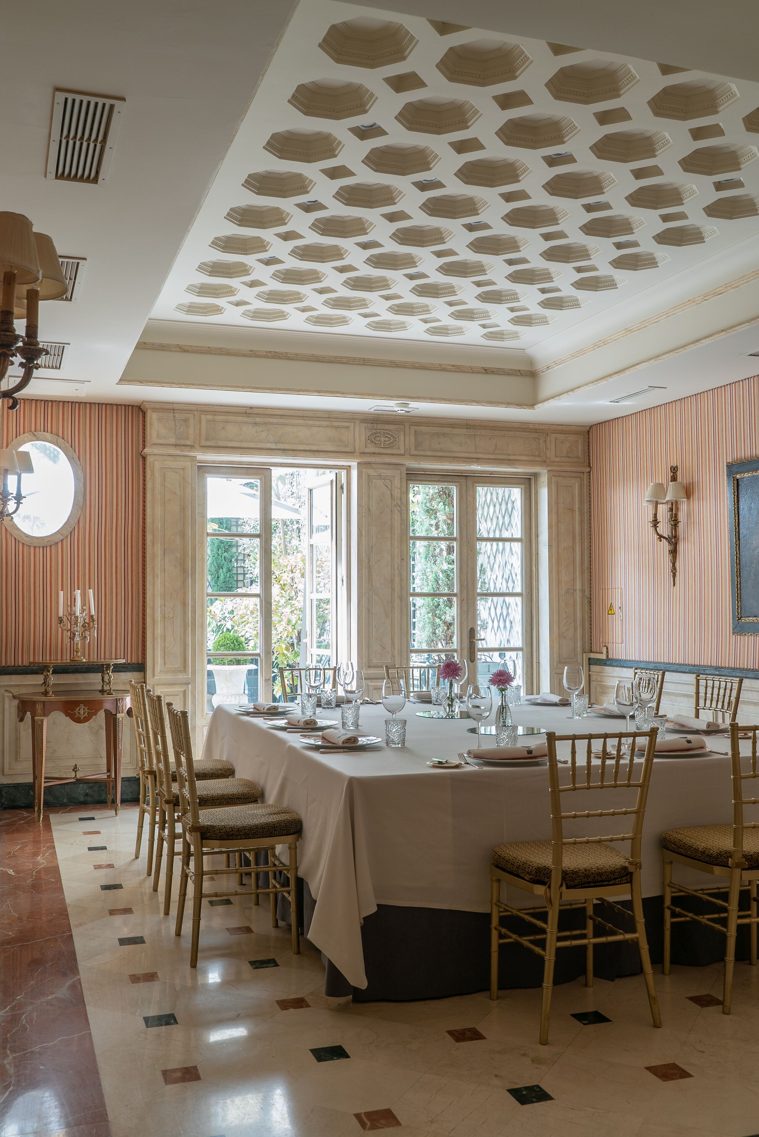 A dining room with a large table set for six, surrounded by six chairs, with a large window providing natural light.