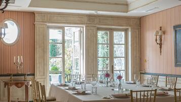 A dining room with a large table set for six, surrounded by six chairs, with a large window providing natural light.