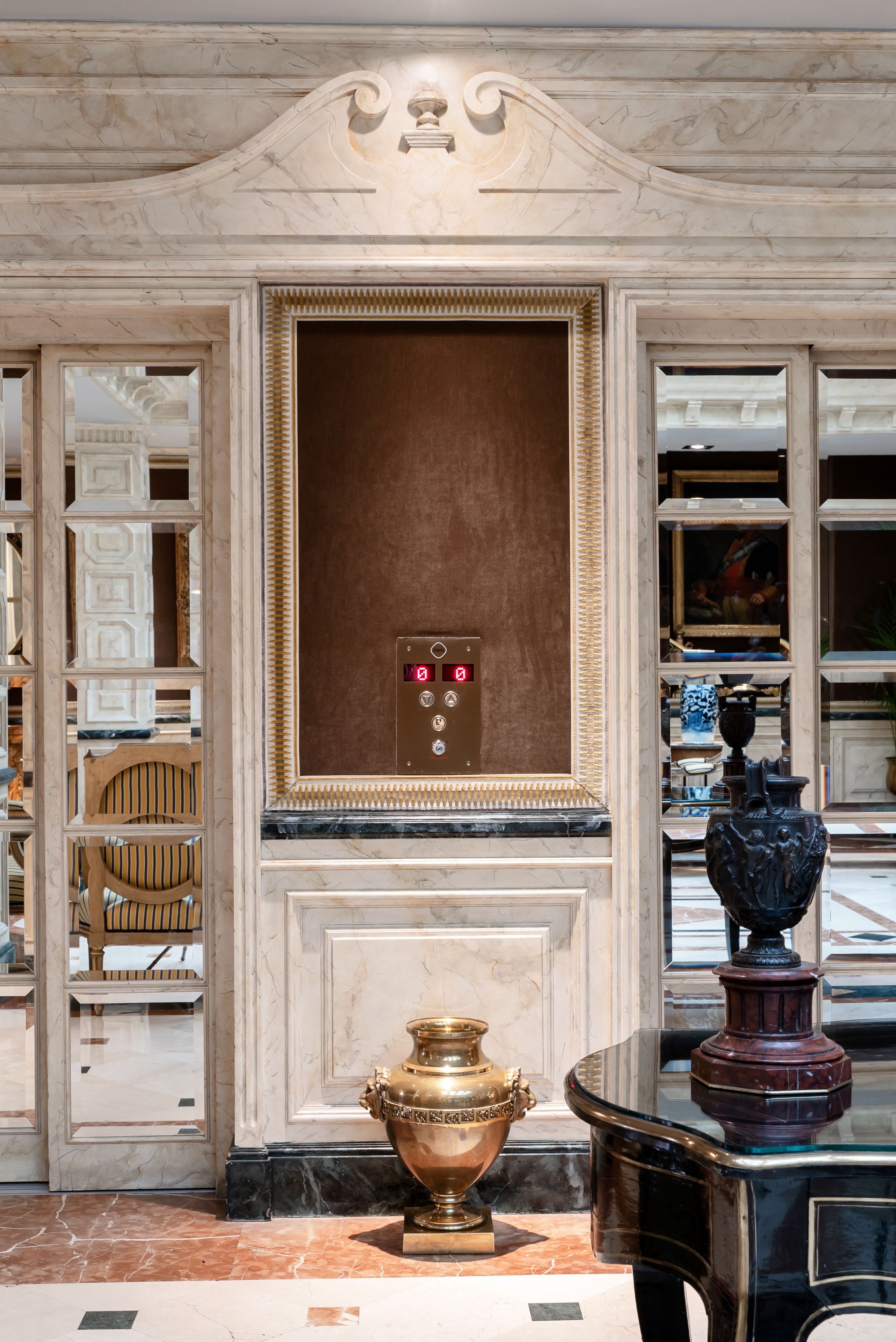 A lobby with a marble wall, a large urn, and a statue.