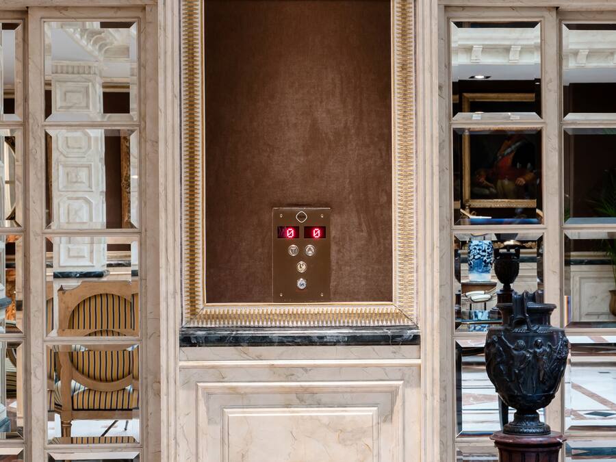 A lobby with a marble wall, a large urn, and a statue.