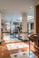 Un vestíbulo espacioso con piso de mármol, un área de comedor central y columnas decorativas.