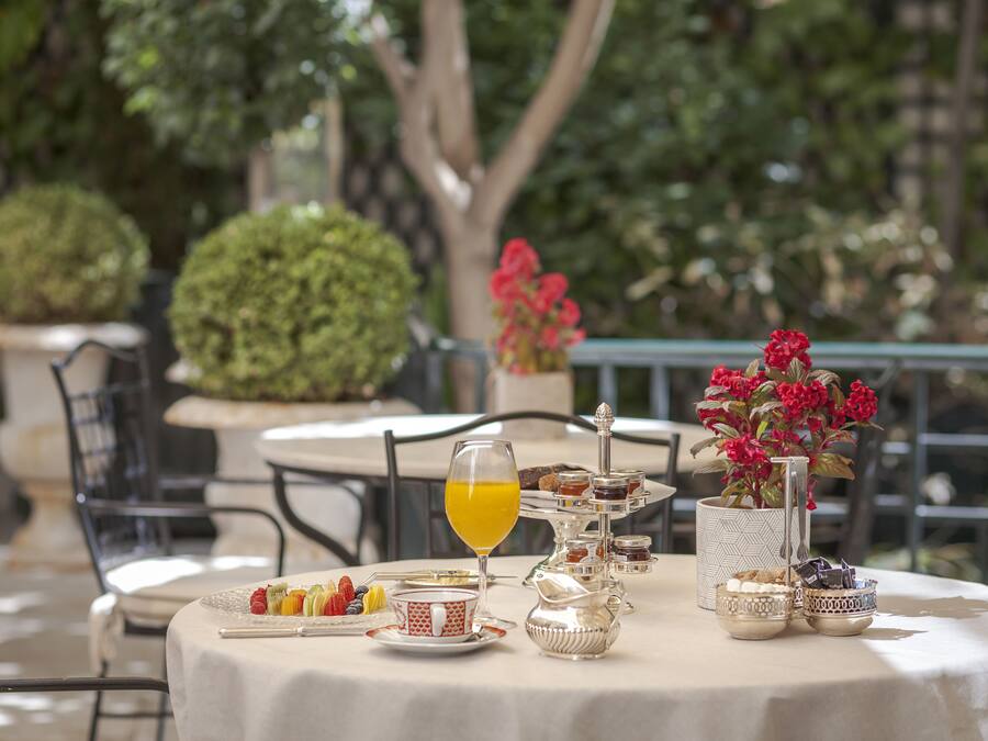 Una mesa dispuesta para el desayuno, con diversos alimentos, un vaso de jugo de naranja y un jarrón de flores rojas.