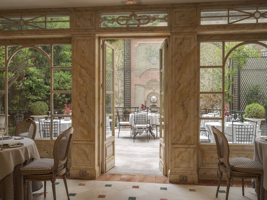 An elegant dining area with marble-paneled walls, large arched windows, and a view of the garden.