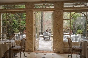 Un elegante comedor con paredes revestidas de mármol, ventanas arqueadas grandes y vistas al jardín.