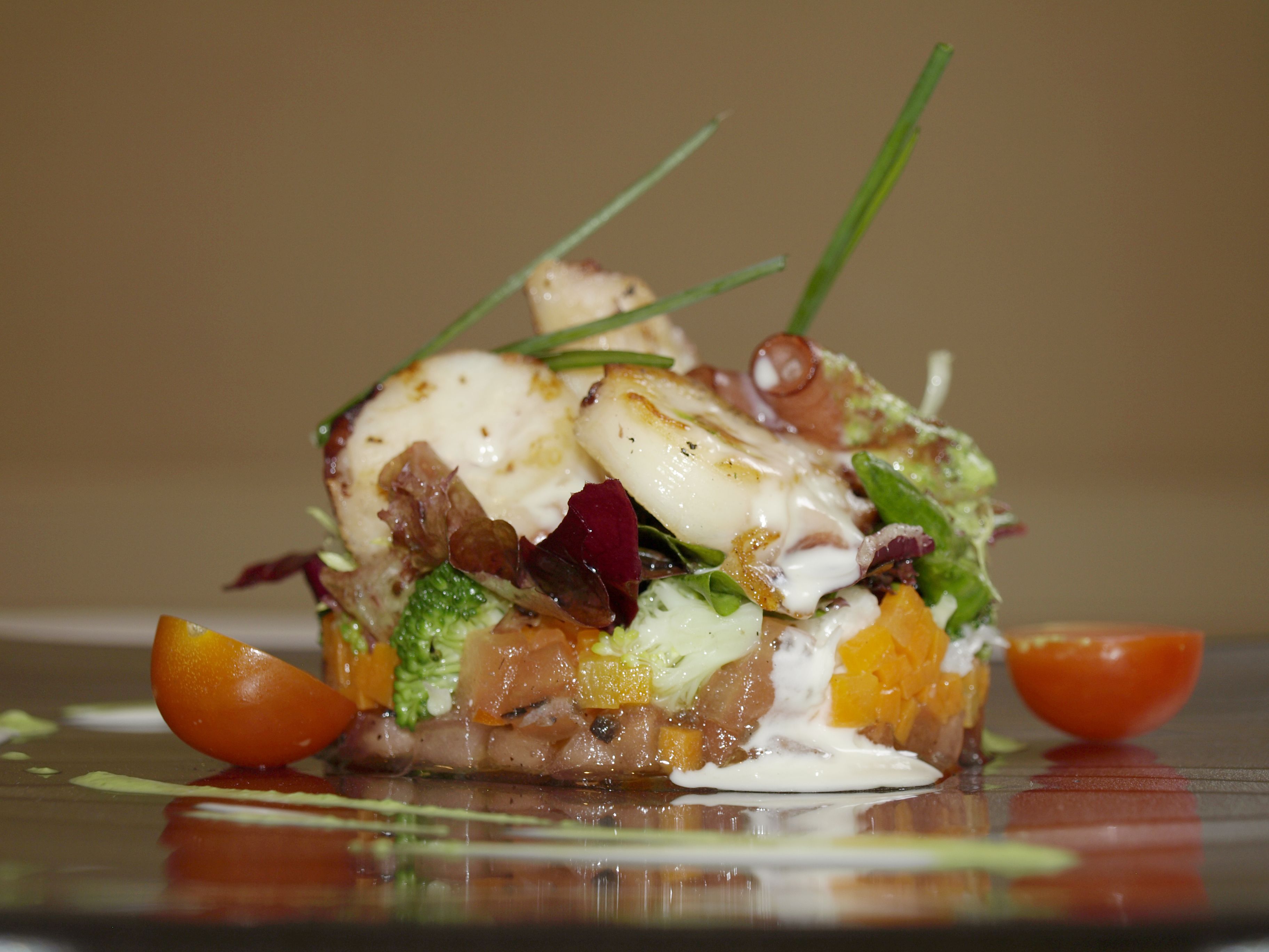 A plated dish with various ingredients, including vegetables and a creamy topping, presented on a reflective surface.