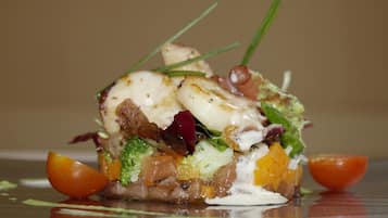 A plated dish with various ingredients, including vegetables and a creamy topping, presented on a reflective surface.