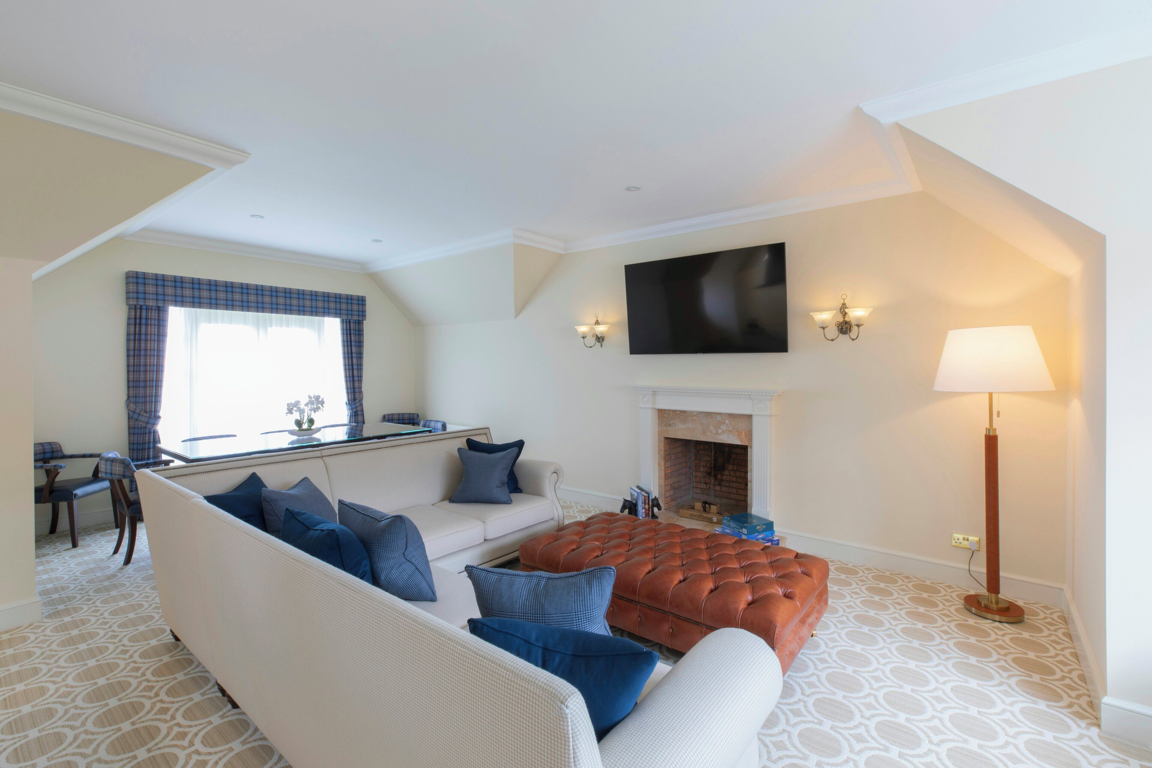 A living room with a sofa, ottoman, fireplace, flat-screen TV, and a lamp.
