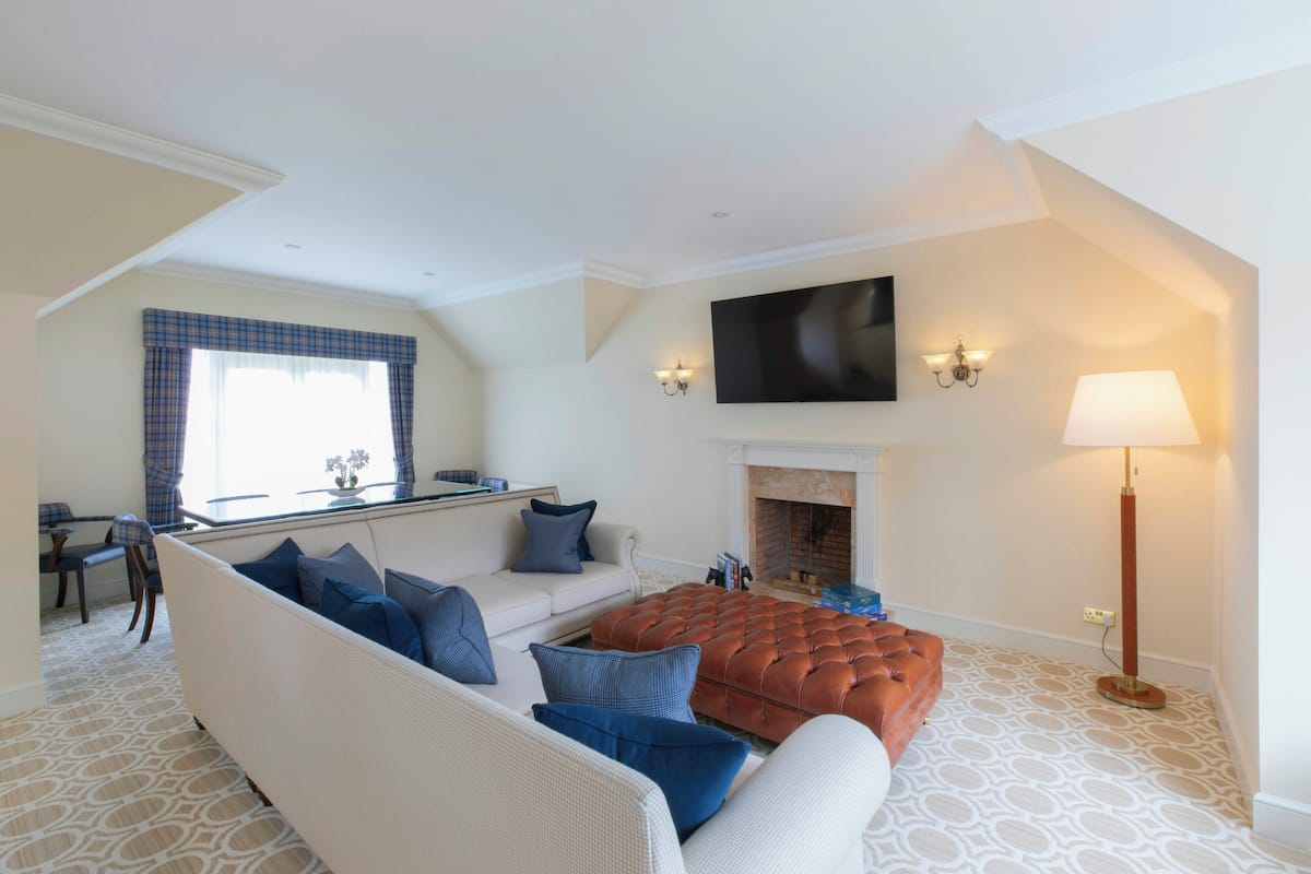 A living room with a sofa, ottoman, fireplace, flat-screen TV, and a lamp.